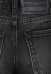Jeans in denim nero con una superficie strutturata, design a cinque tasche e un'etichetta con il marchio e le informazioni per la cura sulla vita posteriore.