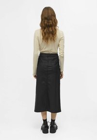 Black denim midi skirt with a straight cut, back pockets, and a high waist, paired with a textured beige ribbed sweater and chunky black shoes.