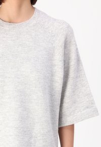 Šedý krátký rukáv pletený svetr s kulatým výstřihem a raglánovými rukávy. Měkká textura, lehký materiál a minimalistický design.