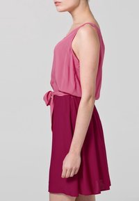 Vaaleanpunainen hihaton mekko, jossa on istuva yläosa ja levenevä hame, jossa on vyötäröllä säätösolki. Hameen väriasteikko siirtyy tummempaan sävyyn.