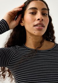 Top a maniche lunghe a righe bianche e nere con scollo rotondo, design aderente e tessuto testurizzato. Cuciture visibili sulle spalle e accenti sottili.