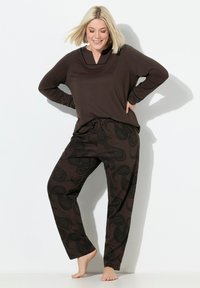 Maglia marrone a maniche lunghe con scollo a V e bordo a contrasto, abbinata a pantaloni marroni larghi con un motivo paisley nero.