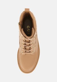 Stivaletto in pelle tan con hardware dorato, punta rotonda e design con lacci. Presenta un motivo trapuntato e una linguetta sul retro.