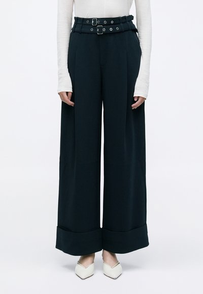 Dark teal wide-leg trousers with a high waist, belted at the top with two belts. Fabric is smooth with a structured silhouette and large cuffs.