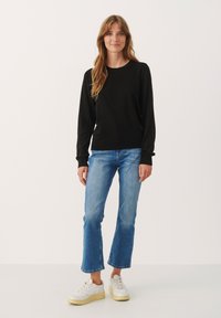 Sort langærmet sweater med rund halsudskæring, parret med lyseblå cropped jeans og hvide sneakers med en cremegul sål.