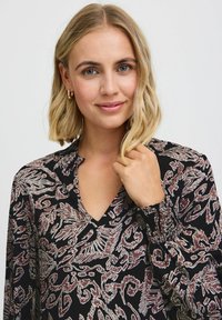 Blusa nera con scollatura a V, maniche lunghe e polsini arricciati. Presenta un motivo floreale in tonalità di bordeaux e crema. Tessuto leggero.