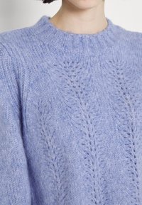 Light lavender knitted sweater featuring a round neckline and leaf-patterned texture. Soft, fuzzy material with ribbed detailing.