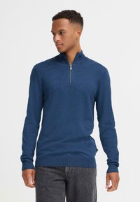 Mørkeblå zip-genser med høy krage, ribbede mansjetter og kant. Glatt tekstur, kroppsnær design og subtile mønsterdetaljer gjennom hele.