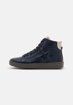 Marineblå high-top sneakers med stjernedesign, sorte snørebånd, beige ankelskærm og brun sål mod en lys grå baggrund.