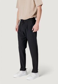 Zwarte, lichte joggerbroek met een elastische tailleband en trekkoord. Gladde textuur, taps toelopende pasvorm, gecombineerd met witte sneakers.