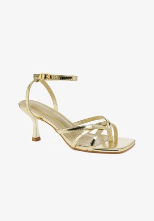 Goldfarbene Riemchen-Hochsandale mit quadratischer Spitze, dünnem Knöchelriemen mit Schnalle und niedrigem Kitten-Heel auf weißem Hintergrund.