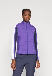 Veste rembourrée violette avec un col montant et une fermeture éclair. Présente des panneaux de couleur contrastante sur les manches et des détails en tissu texturé.
