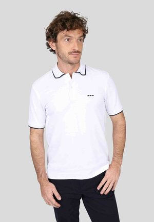 Polo blanc avec des accents noirs, manches courtes et une patte de boutonnage à trois boutons. Logo sur la poitrine gauche. Le matériau semble lisse et respirant.