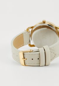 Curea de ceas din piele crem deschis, cu accesorii metalice de culoare aurie, având o textură netedă și carcasă rotundă. Se ajustează cu o închidere cu cataramă.
