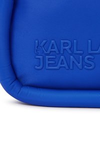 Modrý polstrovaný vak s textúrovaným povrchom, zaoblenými hranami a embosovaným logom "KARL LAGERFELD JEANS". Hladký povrch s kontrastnými detailmi.