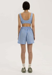 Niebieski i biały prążkowany crop top z otwartych plecach, połączony z dopasowanymi szortami z elastycznym paskiem. Modelka nosi zielone obuwie.