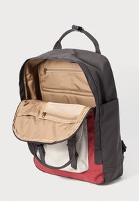Ryggsäck med en mörkgrå utsida, som har ett rymligt, beige-fodrat innervarum, flera fack och ett mjukt handtag.