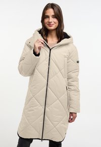 Beige, lange gewatteerde jas met een capuchon, voorzien van een ruitpatroon, een voorrits en zijzakken. Zwarte accenten aan de zoom.
