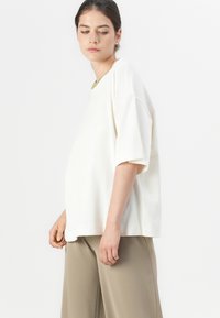 Lossere, kortmouwige top in roomwit met een ronde olijfgroene kraag. Glad textuur en eenvoudig ontwerp, gecombineerd met taupe-kleurige broek.