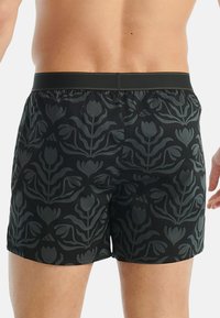 Pantaloni da nuoto neri con motivo floreale tonale, vita elasticizzata e un tessuto liscio e strutturato. Dettagli accentuati includono un sottile logo.