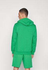 Sweatshirt verde com capucho e um design simples, apresentando um bolso tipo canguru e punhos canelados. Combinado com calções verdes a condizer.