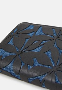 Zwart bloemen snijpatroon op een blauwe denim achtergrond; met soepele leren randen en intrigerende textuurcontrast.