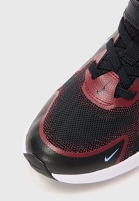 Gros plan sur une sneaker de sport noire et rouge avec un tissu en maille, des lacets noirs, une semelle blanche et de petits logos Nike bleus et noirs.