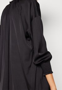 Czarny satynowy top z marszczonym dekoltem, luźnym krojem i ściągaczami na rękawach, prezentujący gładką teksturę i eleganckie drapowania.