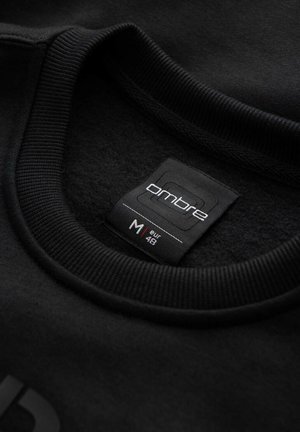 Zwarte sweatshirt met een ronde geribbelde halslijn, zachte textuur en een label met de tekst "ombre", maat M (EUR 48).