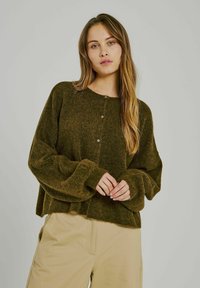 Ciemnozielony, oversize'owy sweter kardigan z długimi rękawami. Posiada okrągły dekolt i zapięcie na guziki. Miękka struktura, lekko skrócony fason.