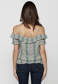 Top con motivo floreale con ruffle sulle spalle, spalline sottili regolabili, in colori chiari con accenti turchesi e marroni; orlo a peplum.