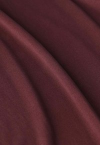 Tissu bordeaux avec une texture lisse, affichant un éclat subtil et un léger motif nervuré, plié pour montrer de la profondeur et de la douceur.