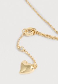 Zlatý retiazkový náhrdelník s príveskom v tvare srdca a malým zirkónovým detailom. Hladký povrch s lesklým leskom.