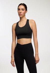 Top corto atletico nero con scollatura tonda e spalline larghe, abbinato a leggings neri a vita alta con dettagli incrociati in vita.