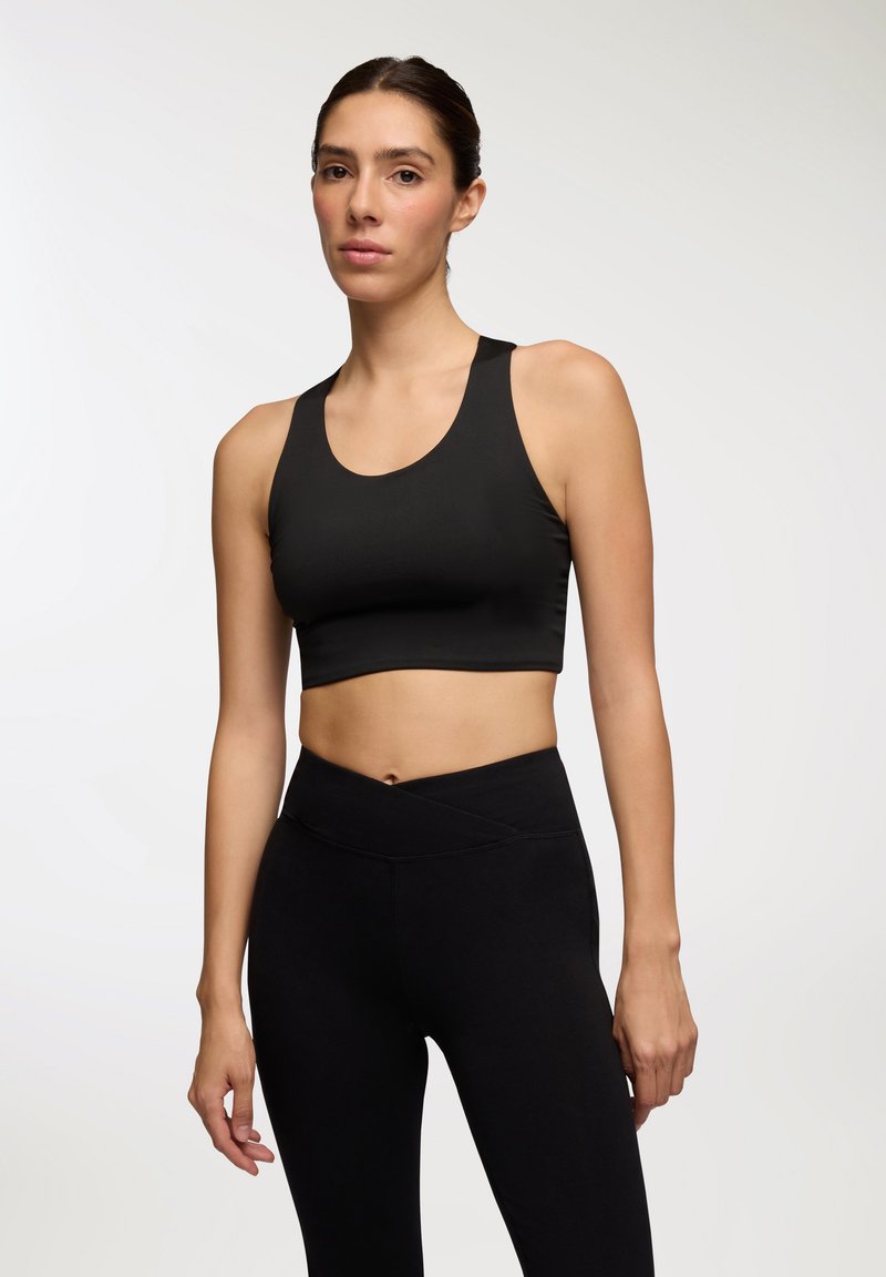 Top corto atletico nero con scollatura tonda e spalline larghe, abbinato a leggings neri a vita alta con dettagli incrociati in vita.