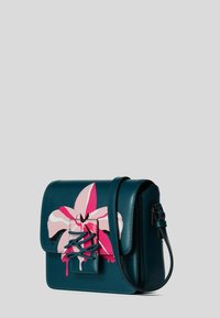 Borsa a spalla in pelle turchese con un grande design floreale rosa e bianco, forma rettangolare e una chiusura decorativa sul davanti.