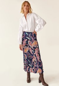 Cămașă albă cu manșete bufante, asortată cu o fustă lungă, plisată de culoare bleumarin, cu modele florale colorate și cizme cu toc maro.