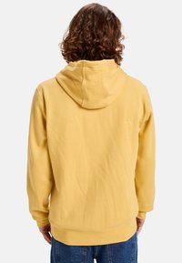 Sudadera amarilla con capucha, de textura suave, con puños y dobladillo acanalados. Presenta un diseño simple sin logotipos o patrones visibles.