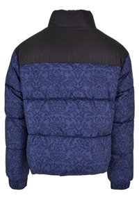 Bunda s kapucňou s čiernym vrchom a tmavomodrou vzorovanou dolnou časťou. Obsahuje prešívanú textúru a elastické manžety. Dizajn s vysokým golierom.