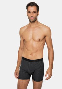 Schwarz-graue gestreifte Boxershorts mit einem weichen Bund, aus leichtem Stoff gefertigt. Das Modell steht mit entspannten Armen an den Seiten.