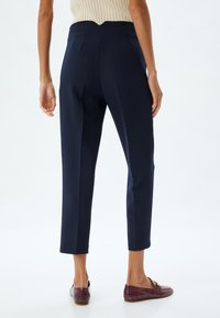 Pantalons taillés bleu marine avec une taille ajustée, texture lisse et longueur courte, associés à des mocassins bordeaux avec une finition texturée.