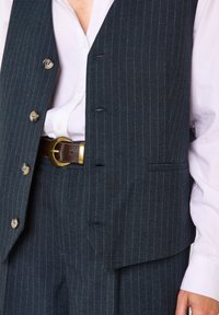 Gilet a righe sottili blu scuro realizzato con tessuto strutturato, caratterizzato da bottoni metallici, una tasca e una camicia bianca a contrasto sotto.