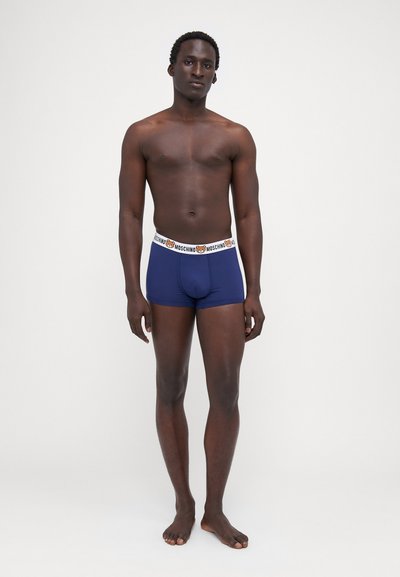 Boxeri scurți de culoare bleumarin cu un brâu alb ce prezintă un logo Moschino și un design cu urs. Confecționați dintr-un material neted și elastic.
