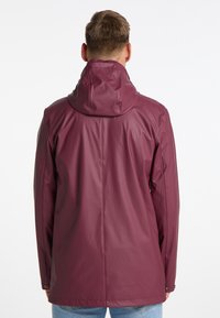 Mørkerød vandtæt jakke med høj krave, der har en glat tekstur og minimalistisk design. Synlige stikninger og knapdetaljer.