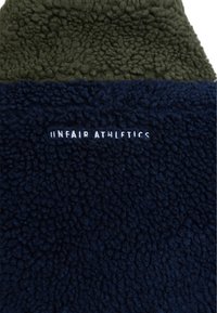 Tissu polaire bicolore vert foncé et bleu marine avec texte brodé blanc "UNFAIR ATHLETICS" sur la section bleu marine.