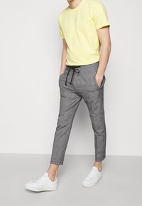 Szare spodnie o fakturowanej powierzchni z wiązaniem w pasie, zestawione z żółtą koszulką i białymi trampkami. Spodnie mają boczne kieszenie i zwężany krój.