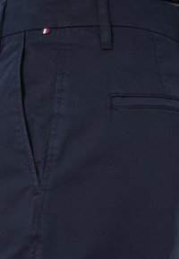 Pantaloni in cotone blu navy con una texture liscia, dotati di una piccola etichetta logo rossa, bianca e blu e una tasca posteriore. Design sartoriale.