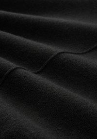 Zwart wollen stof met een fijne textuur, met zachte plooien en een gladde oppervlakte. Het materiaal lijkt dicht en warm.