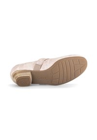 Zapato de ante beige con un tacón bajo y curvado, que cuenta con una suela de goma texturizada y una banda elástica en la parte superior para un ajuste seguro.