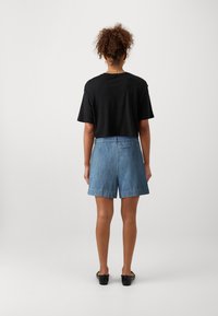 Črna skrajšana majica v kombinaciji s svetlo modrimi denim kratkimi hlačami. Hlače imajo sproščen fit in zavite robove, na voljo pa je tudi ena zadnja žep.